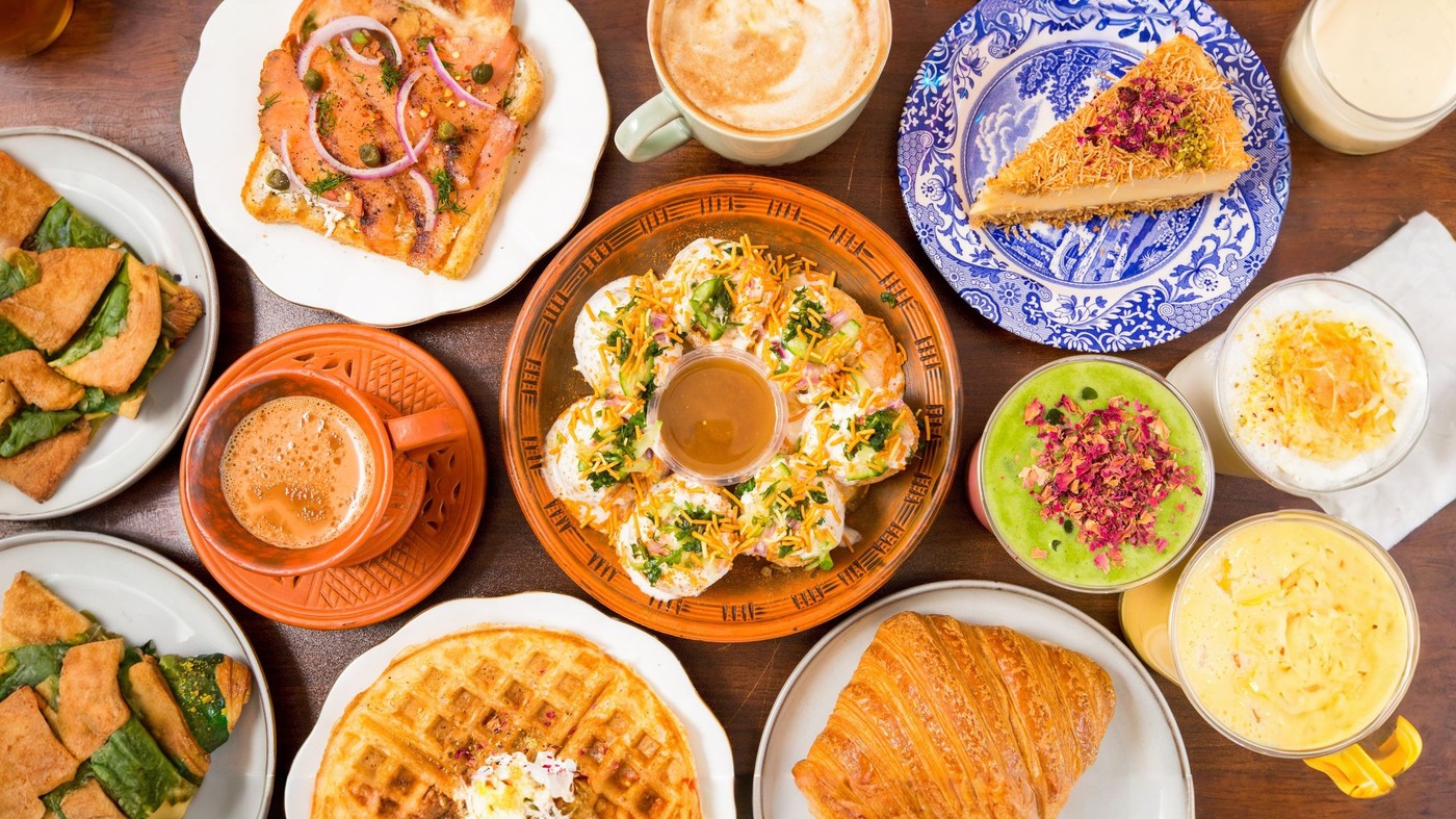 An overhead table of First Cup drinks and food — masala chaa in a clay cup, gulab jamun latte, doi fuska, croissant, matcha